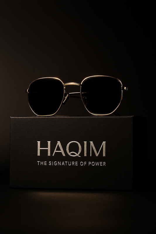 Gold sunglasses on a black box with 'HAQIM' branding against a dark background